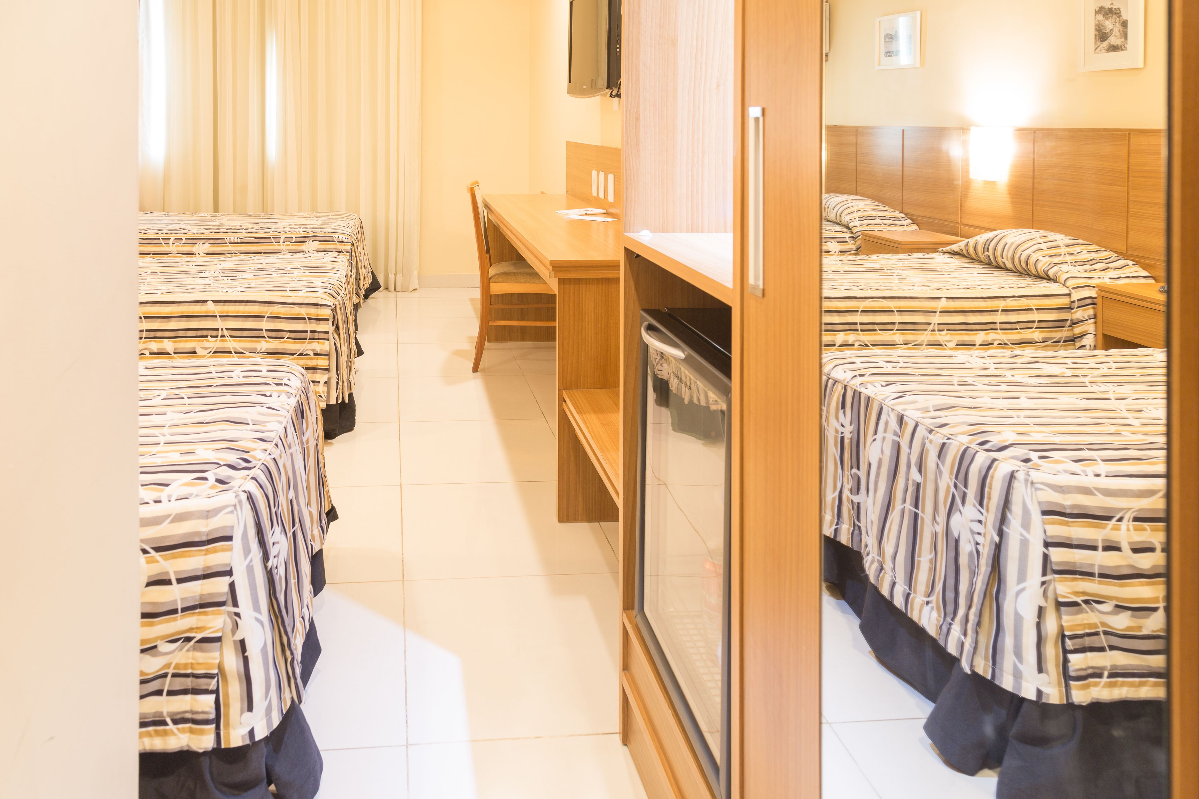 Quarto de hotel com duas camas, uma escrivaninha e uma televisão.