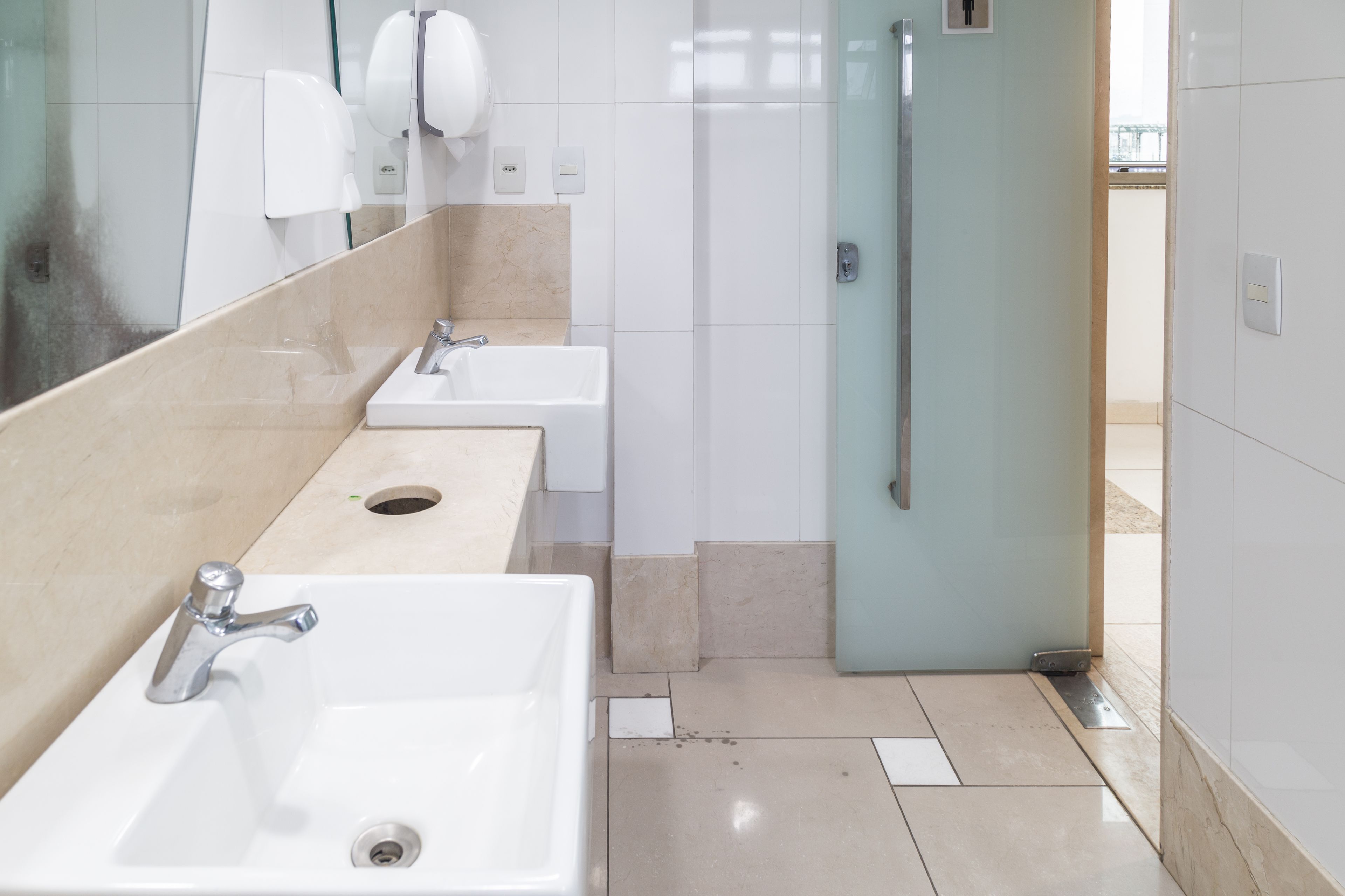 Un baño moderno con tres lavamanos, un secador de manos y una cabina de ducha con paredes de vidrio.