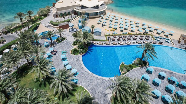 Un resort con una piscina grande, zona de descanso en la playa y vistas al océano.