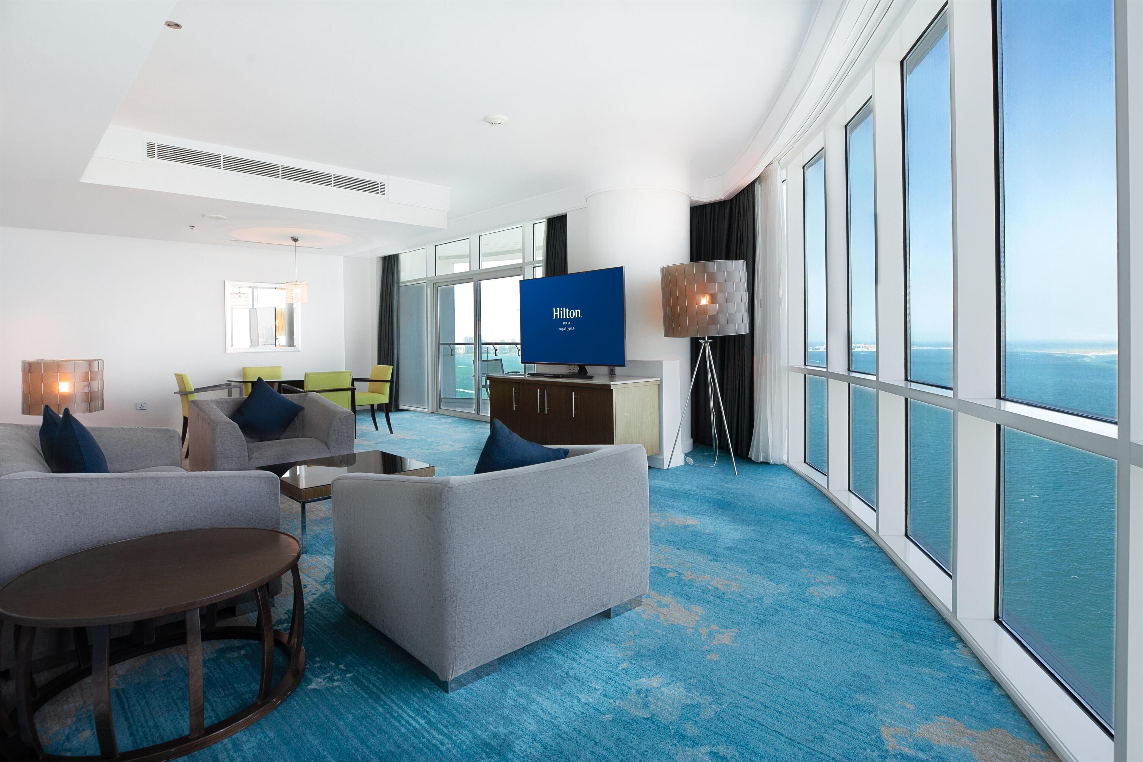 A modern hotel room with a large window, a flat-screen TV, and a seating area with a coffee table.