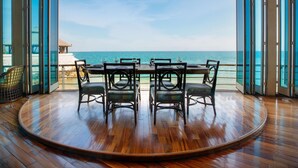 Una mesa de madera redonda con sillas orientadas a un amplio ventanal con vistas al océano.