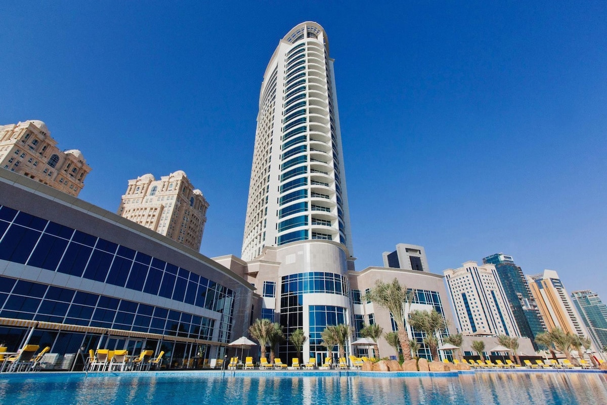 A modern hotel with a pool area, surrounded by high-rise buildings.