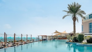 A pool area with lounge chairs, umbrellas, and a palm tree.