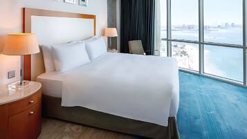 Una camera d'albergo con un letto grande, due lampade ai lati del letto, un comodino, una sedia e vista sulla città attraverso ampie finestre.