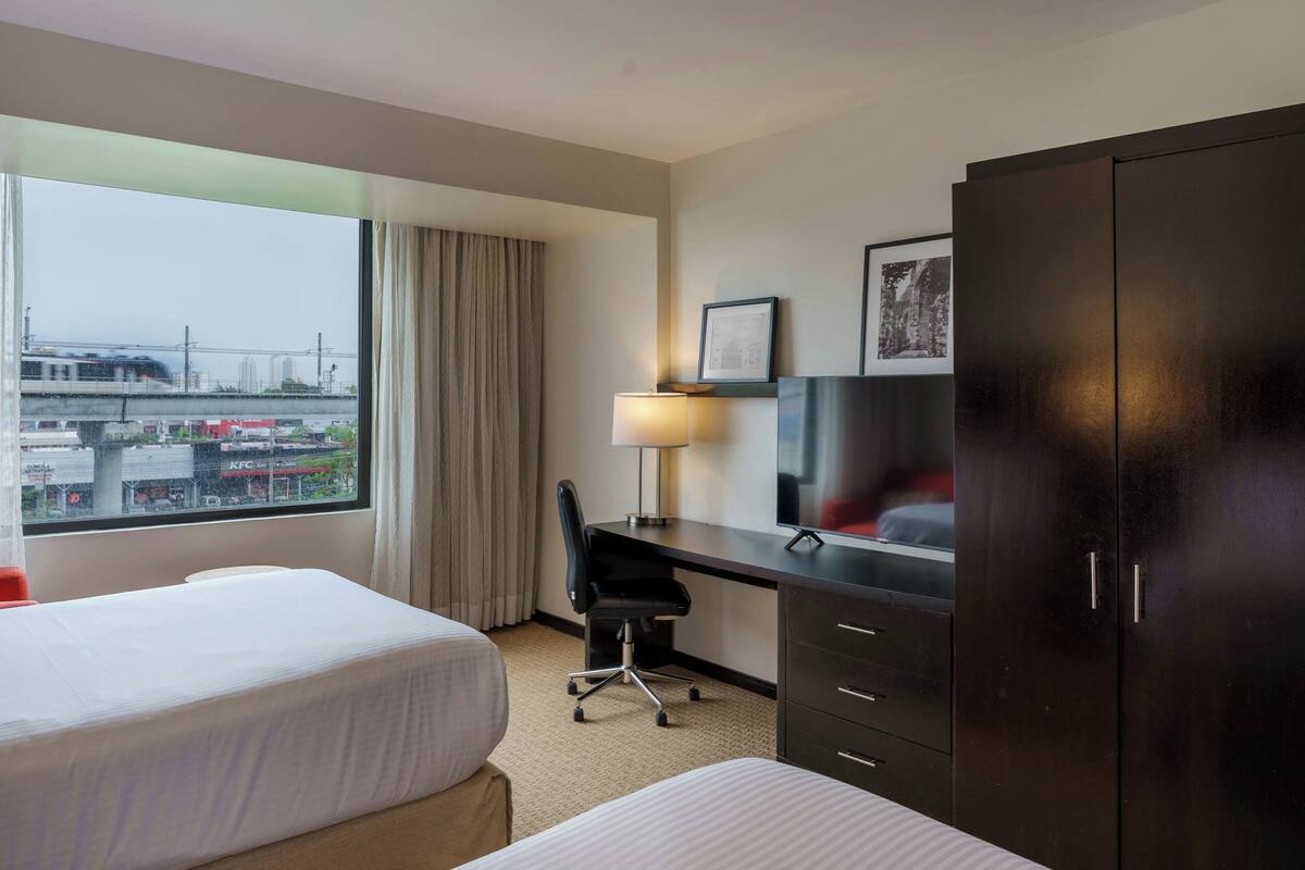 Une chambre d’hôtel avec deux lits, un bureau, une chaise, une télévision et une armoire.