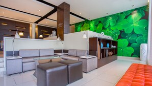 Un moderno vestíbulo de hotel con un sofá seccional, una mesa de centro de vidrio y un mural de pared verde vibrante.