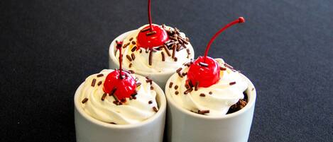 Tres cupcakes con crema batida y cerezas sobre una superficie oscura.