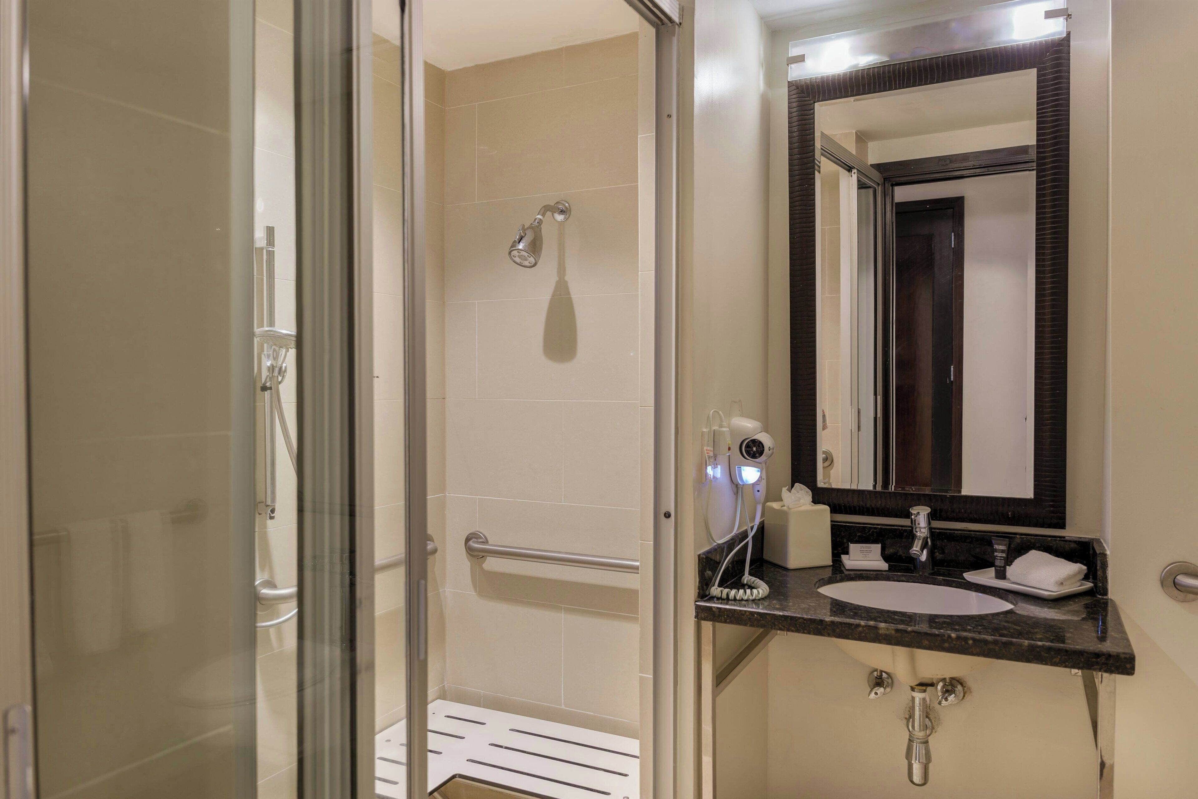 A bathroom with a glass shower enclosure, a sink with a dark countertop, and a mirror with a dark frame.