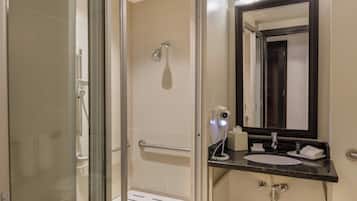 A bathroom with a glass shower enclosure, a sink with a dark countertop, and a mirror with a dark frame.