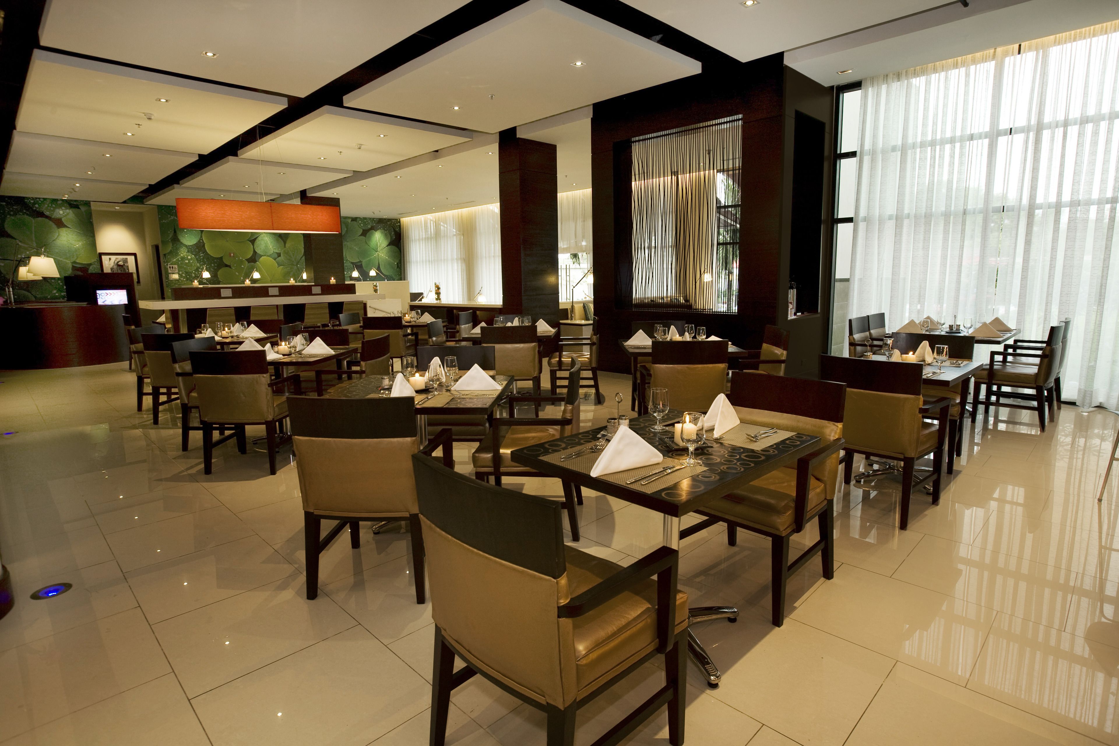 Un restaurante espacioso con varias mesas y sillas, una zona de recepción y amplias ventanas con cortinas.