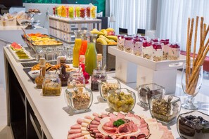 Un bufé con diversas opciones de comida, incluyendo frutas, jugos y quesos.
