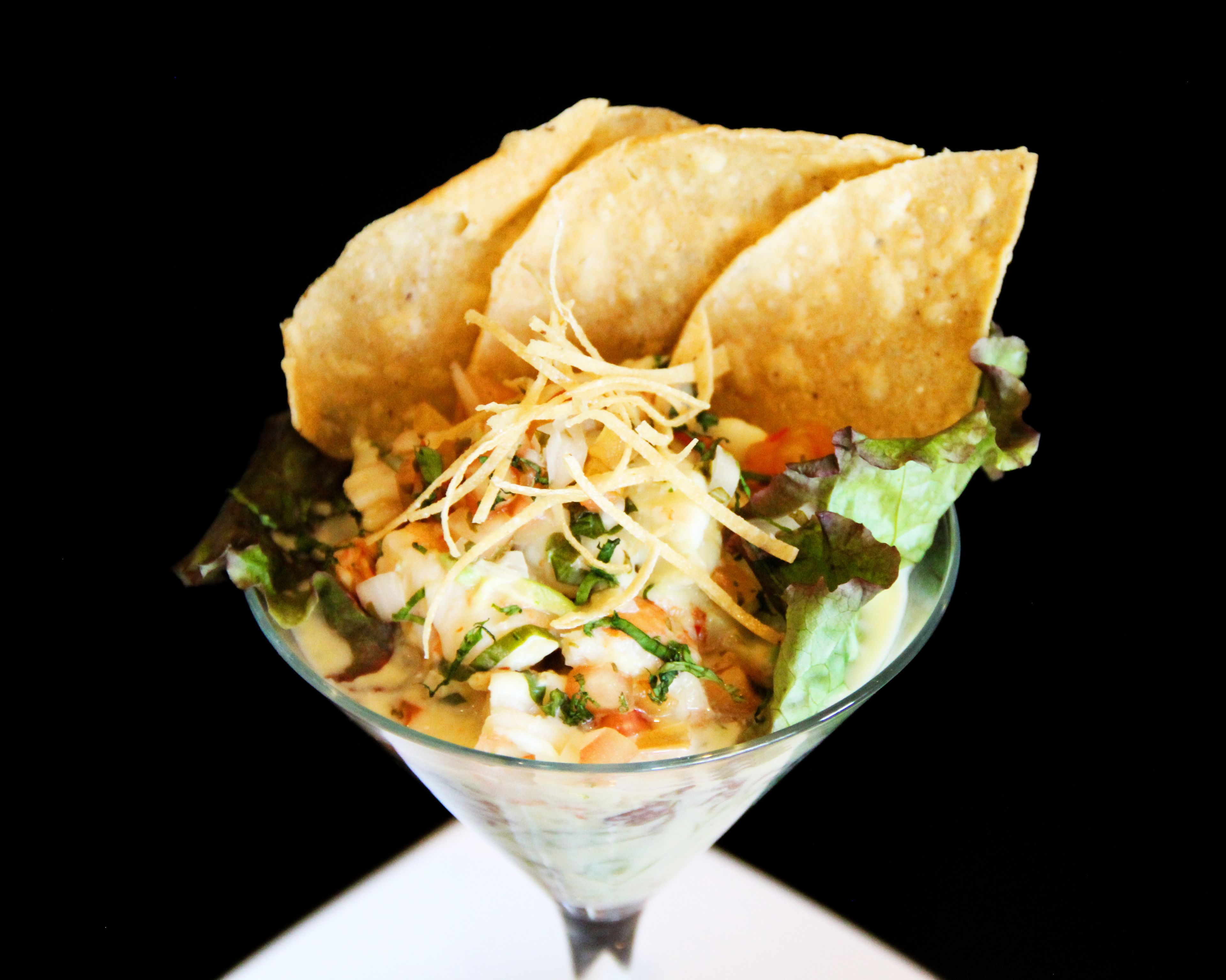 A glass bowl with a salad, shredded cheese, and tortilla chips.
