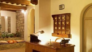 A wooden desk with a lamp, a decorative cabinet, and a patterned rug in a warmly lit room with stone walls and wooden beams. - Country House La Locanda del Borgo (Pietralunga)
