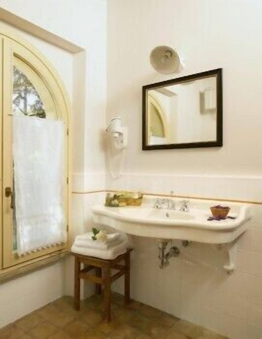A bathroom with a white sink, a mirror, and a towel on a wooden stool.