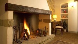 A stone fireplace with a fire, a wooden ceiling, a bookshelf, and a patterned rug. - Country House La Locanda del Borgo (Pietralunga)