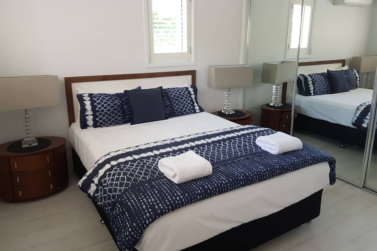 A neatly made bed with a patterned bedspread, two bedside tables with lamps, and a large mirror on the wall.