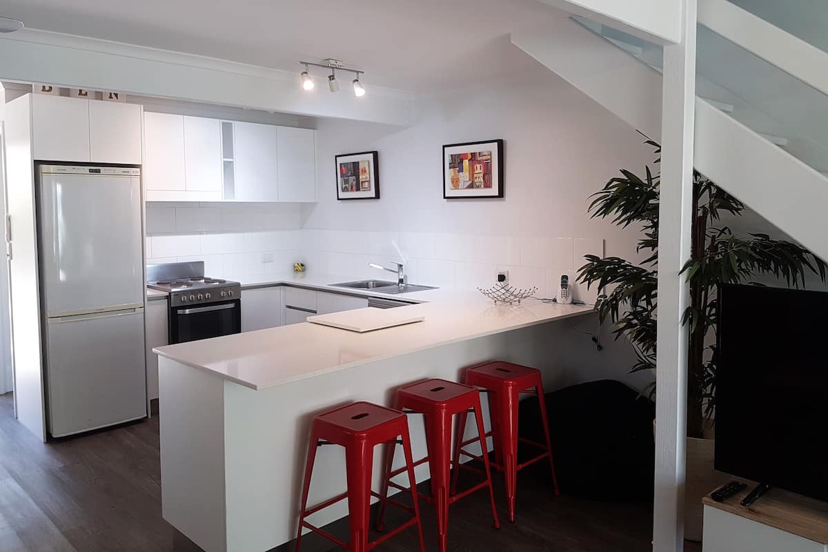 A modern kitchen with white cabinets, a central island with red bar stools, a refrigerator, and a stove.
