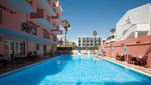 A swimming pool with lounge chairs and tables, surrounded by multi-story buildings with balconies. - Hotel San Marco (Alghero)