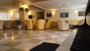 Amplia sala de estar con suelo a cuadros, varios sofás, un piano y plantas decorativas.