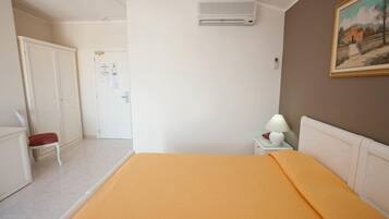 Una camera da letto con un letto, un comodino con una lampada, un condizionatore d'aria, una porta e un quadro appeso al muro.