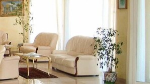A spacious living room with a large window, a sofa set, a coffee table, and a potted plant. - Hotel San Marco (Alghero)