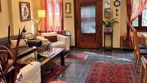 A living room with a sofa, a coffee table, and a red ottoman. There is a door with a window and curtains, and a wall clock. - Ahmet Efendi Evi (Istanbul)