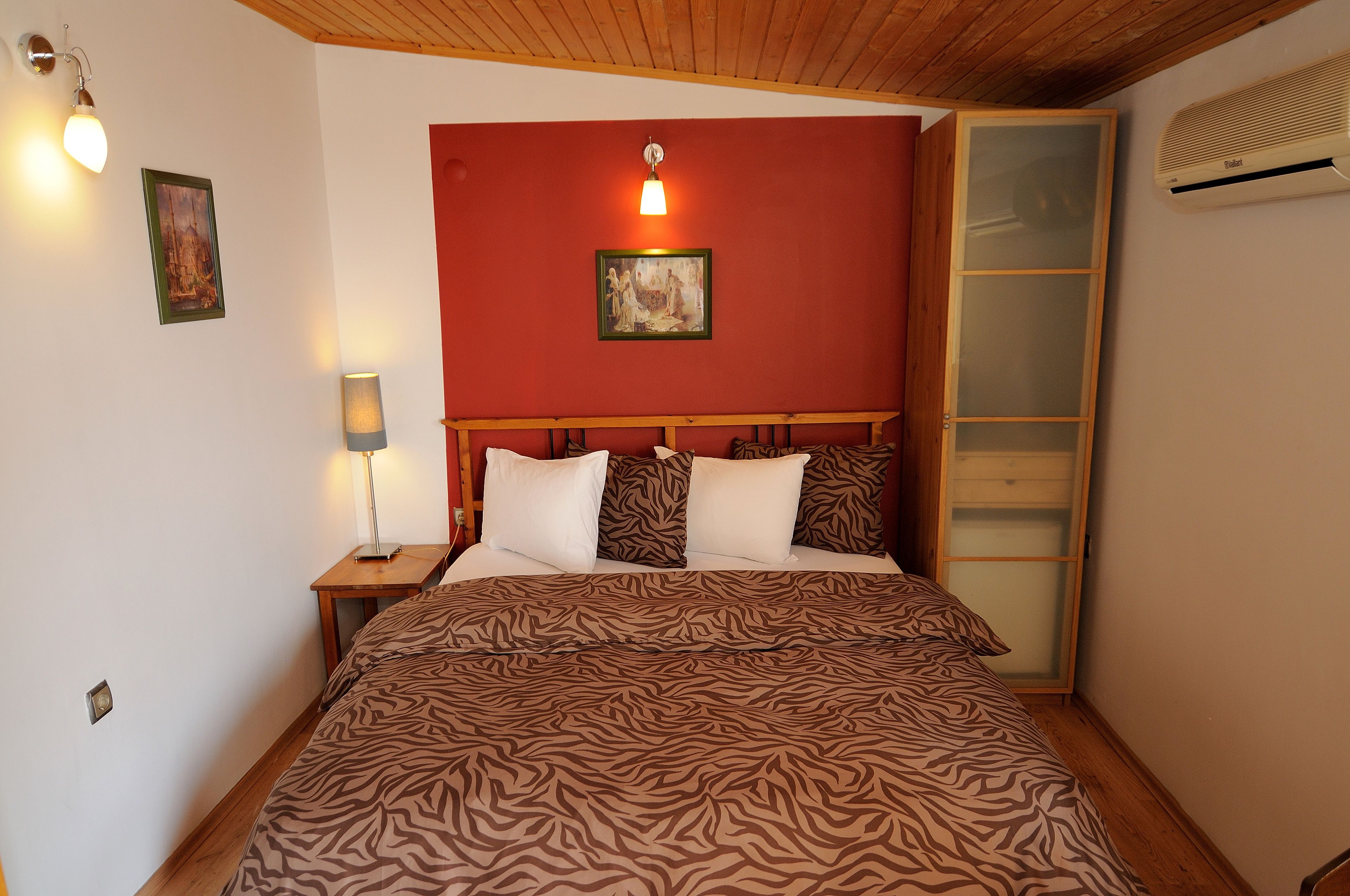 A bedroom with a zebra-patterned bedspread, a wooden headboard, a nightstand with a lamp, and a painting on the wall.