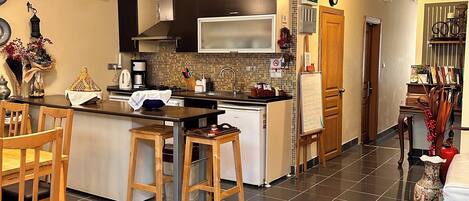 A modern kitchen with a central island, wooden stools, and a red patterned rug.
