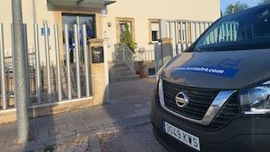 Fachada de un edificio con una camioneta Nissan estacionada frente a él, banderas y una reja metálica.