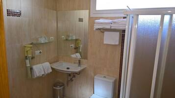 Un baño con lavamanos, espejo e inodoro. Hay toallas en un perchero y una puerta de ducha.