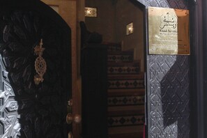 A dark wooden door with intricate carvings and a brass plaque with text. - Riad Nesma Suites & SPA (Marrakech)