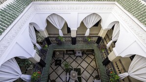 A courtyard with a tiled floor, a central table, and potted plants. - Riad Nesma Suites & SPA (Marrakech)