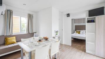 Une pièce moderne et bien éclairée, comprenant une table à manger, des chaises, un canapé avec des coussins, un lit et un téléviseur fixé au mur.