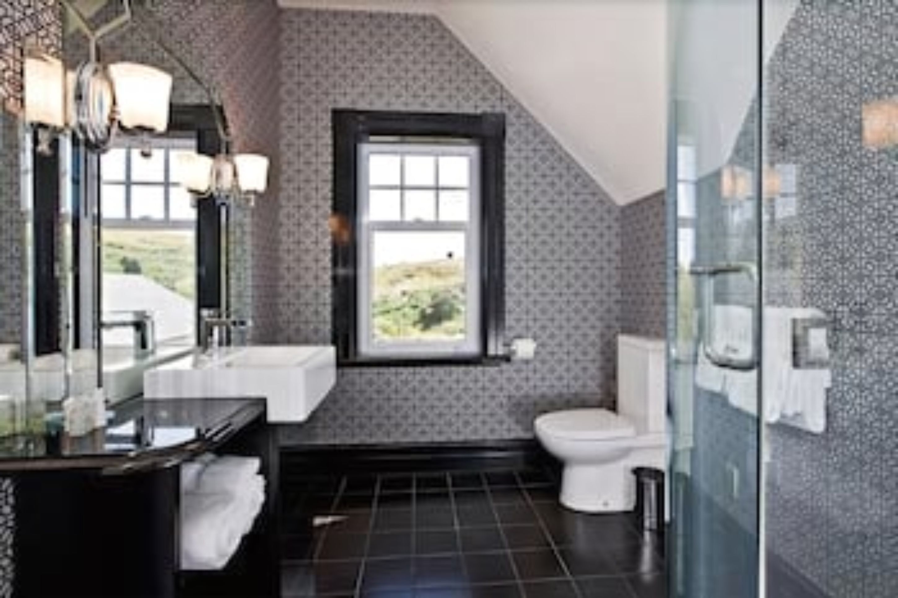 A modern bathroom with a large mirror, a sink, and a toilet.