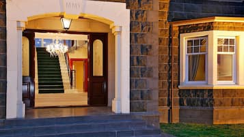 Entrada de hotel com fachada de pedra, uma escadaria e um candelabro.