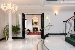 Un lobby espacioso con piso de mármol, una lámpara de araña grande, una chimenea y una escalera.