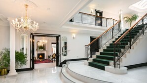 En imponerende foyer med et marmorgulv, en trappe med sorte gelændere og en lysekrone.