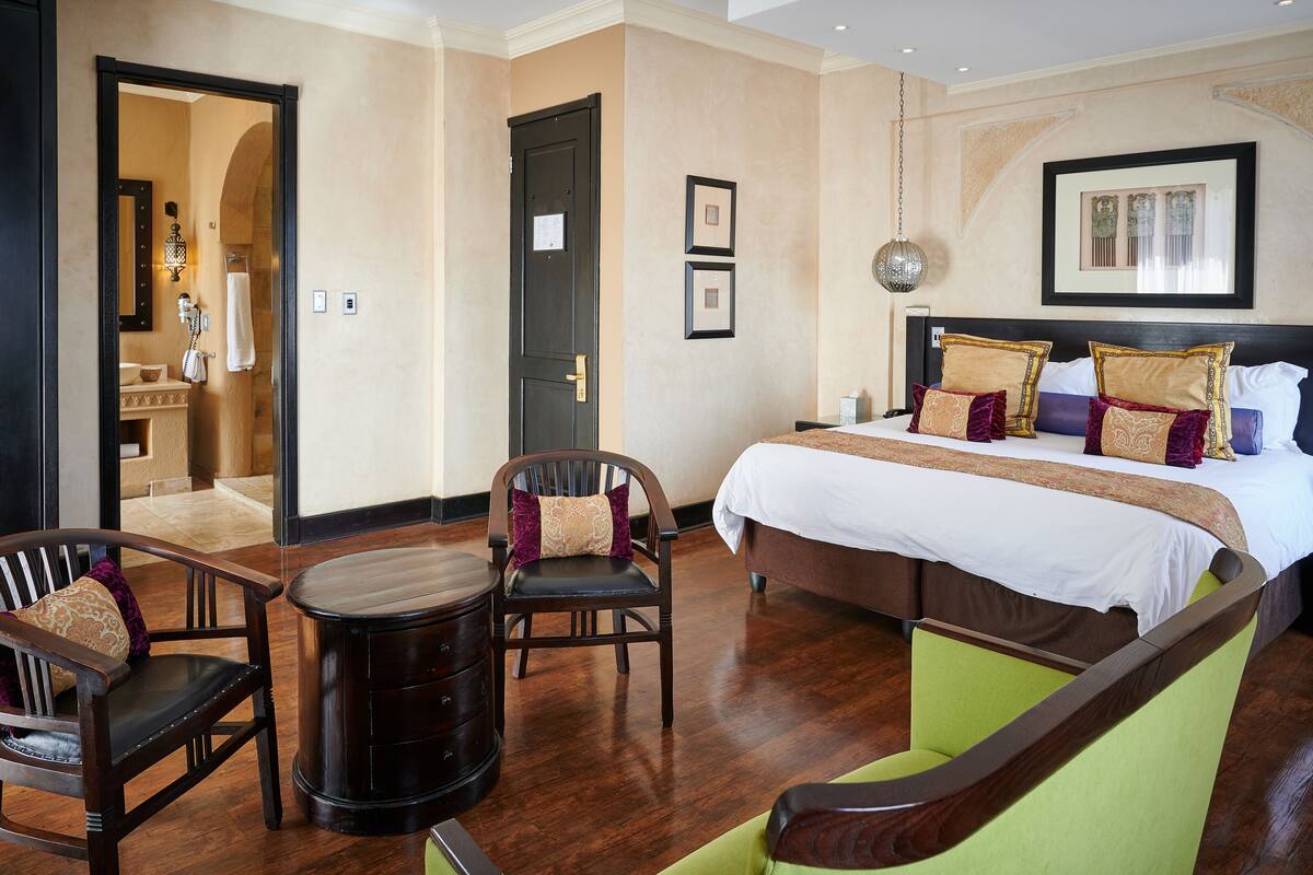 A hotel room with a bed, two chairs, a small table, and a mirror.