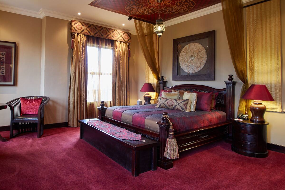 A spacious bedroom with a large bed, a sitting area with a chair, and a decorative ceiling.