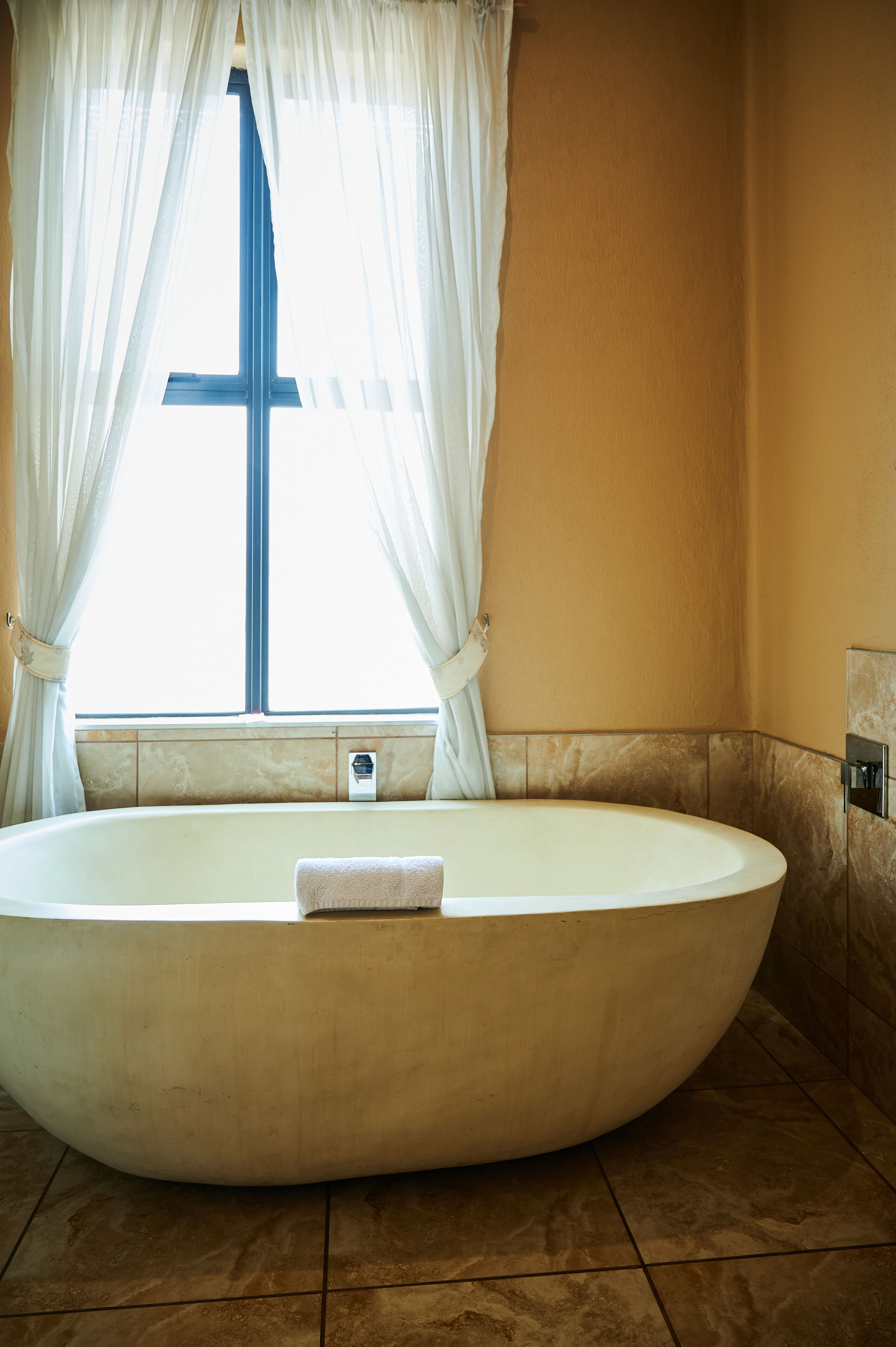 Una bañera grande y separada en un baño con ventana y cortinas.