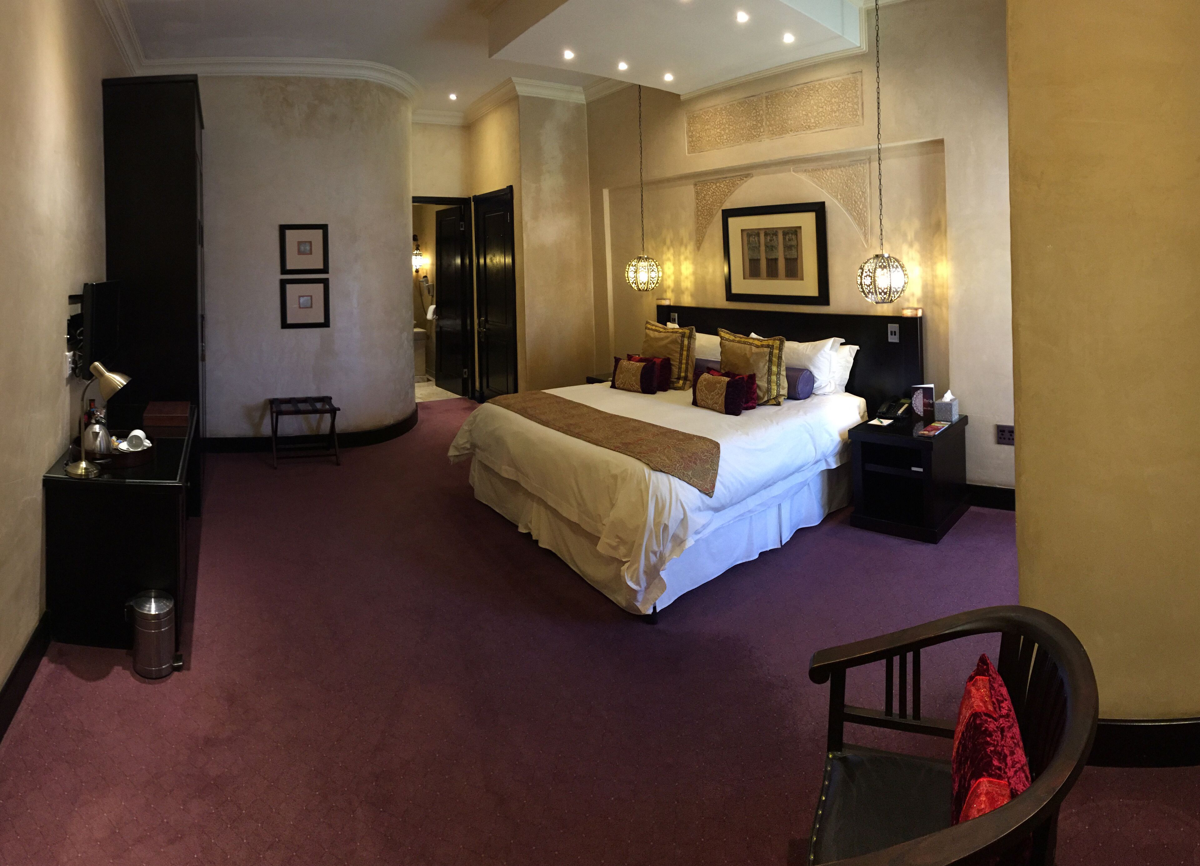 Una habitación de hotel con una cama grande, mesitas de noche, un escritorio con lámpara y una silla.