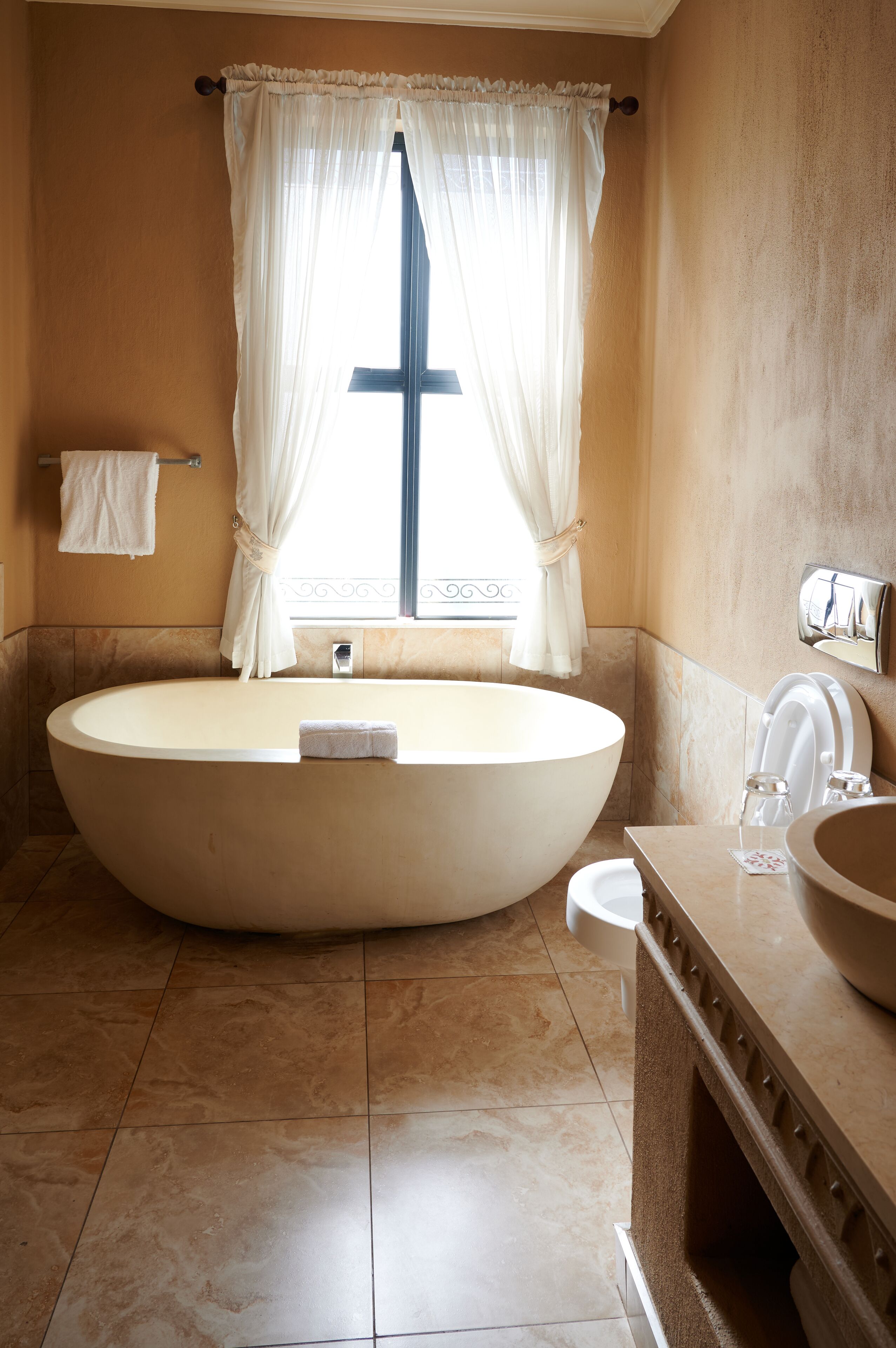 A large freestanding bathtub in a bathroom with a window and a towel rack.