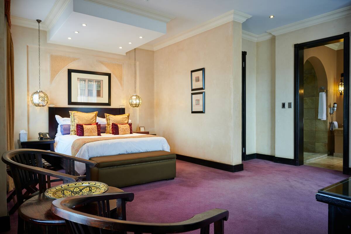A hotel room with a large bed, two bedside tables, a seating area with chairs, and a large mirror.