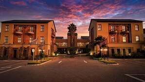 A hotel with a central courtyard, featuring a symmetrical facade with multiple balconies, a prominent palm tree, and a brick entrance. - Tayfin Royale Hotel & Restaurant (Centurion)