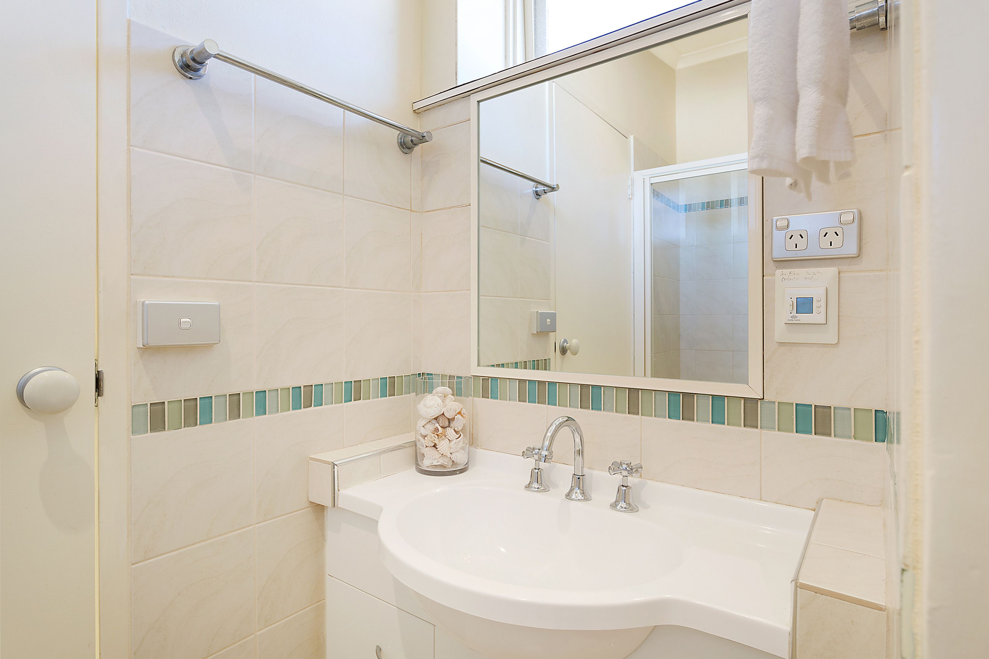 Une salle de bain avec un lavabo blanc, un pot en verre contenant des articles de toilette, un miroir et un porte-serviettes.