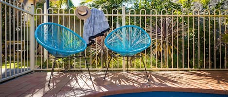 A poolside area with two blue chairs, a white fence, and a pool.