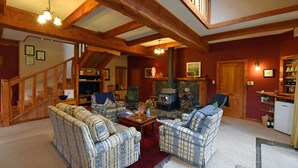 A cozy living room with wooden beams, plaid sofas, a fireplace, and a staircase. - Murchison Lodge (Murchison)