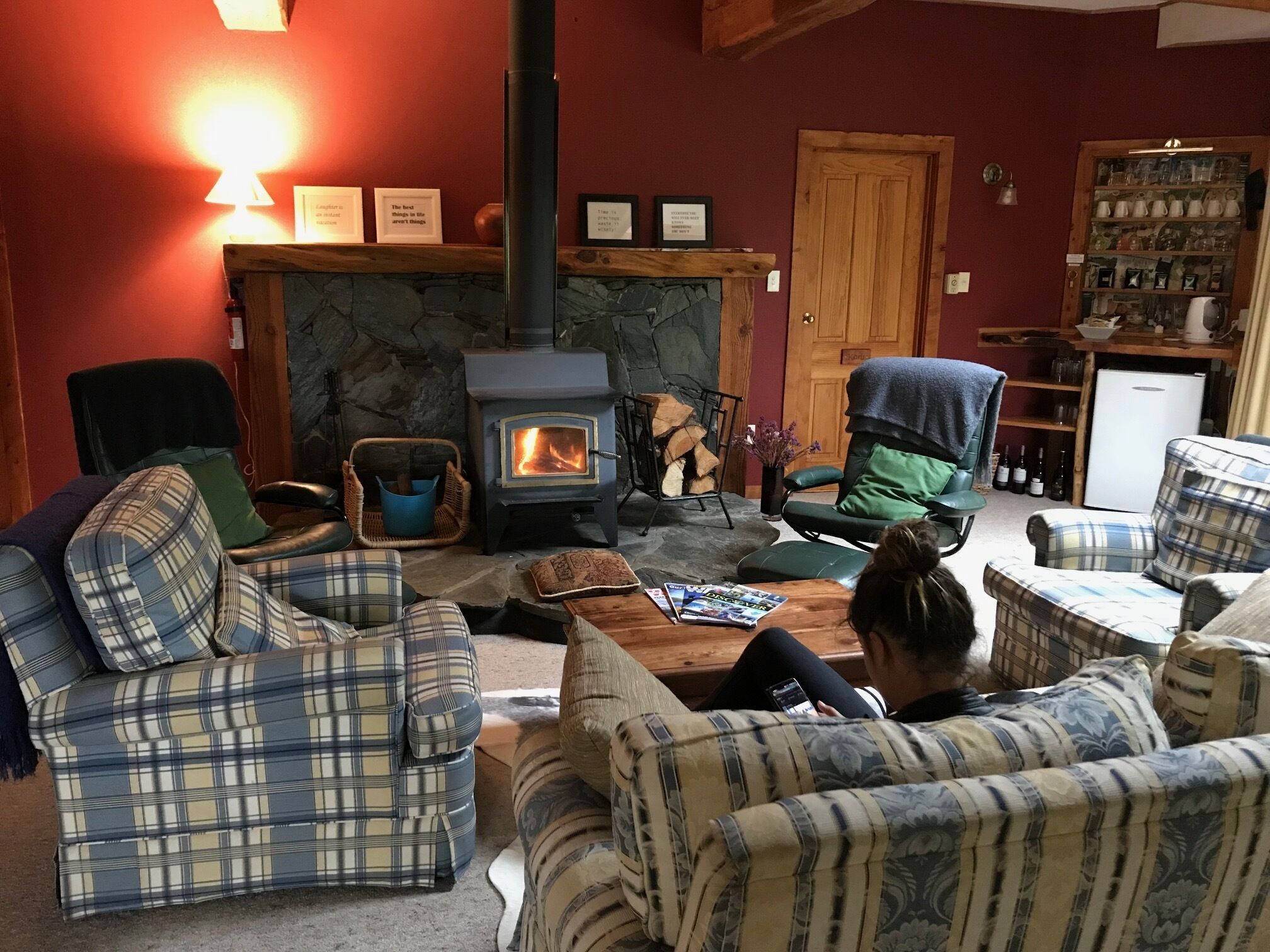 A cozy living room with plaid furniture, a stone fireplace, and a wood-burning stove.