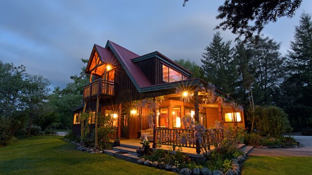 A two-story wooden house with a balcony, a porch with outdoor lighting, and a well-maintained lawn. - Murchison Lodge (Murchison)