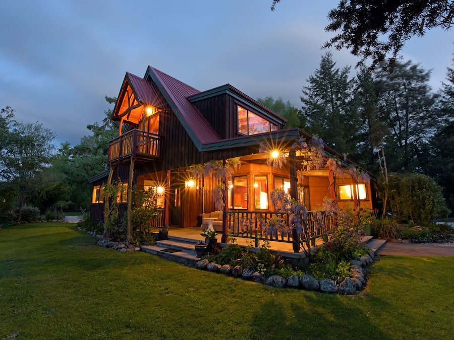 Une maison en bois à deux étages, dotée d’un balcon, d’un porche avec éclairage extérieur et d’une pelouse bien entretenue.
